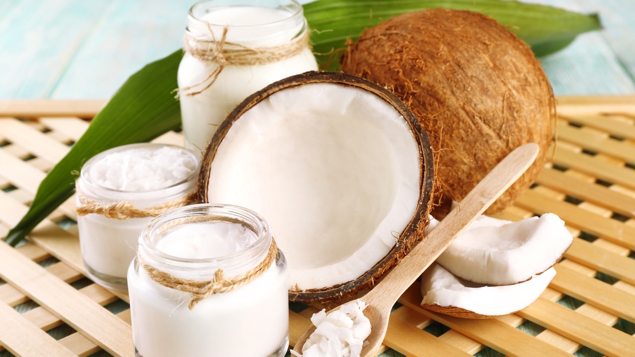 Fresh coconut oil in glassware on color wooden table and grid tray background