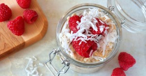 Healthy breakfast refrigerator oatmeal with fresh raspberries and shredded coconut in a glass jar, downward view on white granite